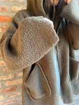 Campera de corderito color verde oscuro, con diseño holgado, cuello alto y manga larga. Presenta una etiqueta de cuero sintético en la manga.