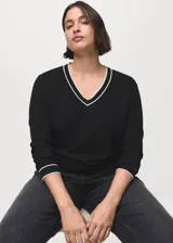 Jersey de punto fino de manga larga en color negro, con cuello en V y detalles de líneas blancas en contraste en el cuello y los puños.