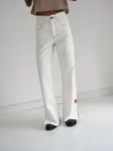 Pantalón vaquero de tiro alto y corte recto, color blanco, con aberturas laterales en los bajos y detalles de terminación en cuero.