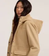 Campera alargada de Blue Steel confeccionada en polivelour, con cuello alto, capucha desmontable, cierre frontal oculto y bolsillos con solapa. Presenta un diseño minimalista y elegante con recortes delanteros.