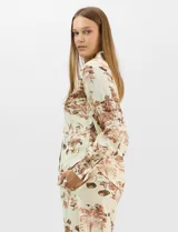 Conjunto de dos piezas compuesto por camisa de manga larga con cuello solapa y botones frontales, y pantalón de tiro alto con pierna recta y bolsillos laterales. Ambas prendas presentan un estampado paisajístico en tonos marrones sobre fondo crema.