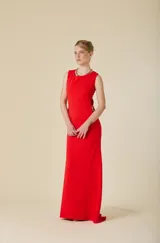 Vestido largo rojo de crêpe elastizado, con silueta ceñida, cuello redondo y aberturas laterales decorativas unidas por pasadores metálicos dorados.