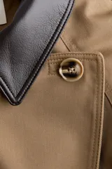 Gabardina corta de sarga color marrón claro, con doble botonadura, cuello de solapa en contraste de color negro con efecto cuero, bolsillos laterales con solapa y cinturón ajustable para anudar en la cintura.