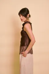 Blusa sin mangas de satén color tostado, con cuello redondo drapeado y detalle asimétrico de encaje en el ruedo.