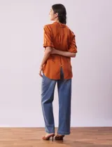 Camisa color beige de tencel, marca Hester & Orchand, con cuello con solapa, escote en V, abertura central con botones y bolsillos delanteros. Las mangas son largas y regulables con presilla y botón.