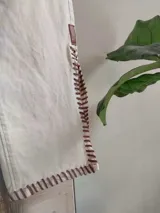 Pantalón de jean blanco con corte acampanado, cintura alta, detalles trenzados y aplicaciones de cuero en la parte inferior.