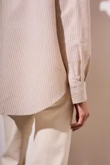 Camisa oversize color arena con rayas verticales marrones, de manga larga y cuello clásico.