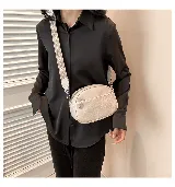 Cartera bandolera color gris claro, de cuero sintético, con correa ancha de tela estampada y cierre superior con cremallera.