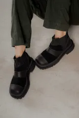 Botas de caña baja con punta cuadrada, confeccionadas en una combinación de cuero liso y gamuza en tonos marrones oscuros. Presentan un diseño de paneles con costuras visibles, elásticos laterales y una suela track robusta.