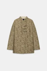 Blazer de corte recto confeccionado en tejido jacquard con diseño floral en tonos tostados. Presenta cuello mao, manga larga y cierre frontal mediante alamares decorativos. Incluye bolsillos de vivo en el delantero.
