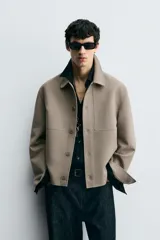 Sobrecamisa color beige de corte cuadrado, con cuello solapa, manga larga con puños abotonados, bolsillos laterales y cierre frontal con botones.