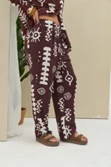 Pantalón de color marrón oscuro con estampado geométrico y tribal en color blanco, de corte recto y tiro medio con cordón ajustable en la cintura.