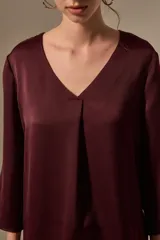 Blusa de satén color bordó con cuello en V y mangas tres cuartos. Presenta un diseño holgado con un pliegue central en el frente.