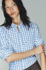 Camisa de manga larga con cuello solapa y cierre frontal de botones. Tejido de popelín 100% algodón con estampado a cuadros azules y blancos. Bajo con corte evasé.