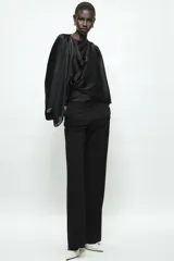 Blusa negra de satén con escote fluido, diseño drapeado en el frente y mangas largas anchas. Presenta un bajo asimétrico y una caída suave y elegante.