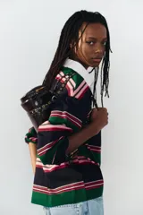 Bolso estilo bowling de cuero sintético acharolado color marrón, con diseño cilíndrico, bolsillos laterales con cierre y doble asa decorada con tachas metálicas doradas.
