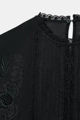 Camisa de algodón con cuello redondo, manga tres cuartos con puño elástico y volante. Presenta detalles de flores bordadas a tono, entredoses y cierre posterior con abertura y botón.