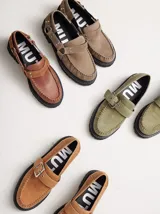 Mocasines de cuero color gris oscuro con diseño de costura en el empeine, ajuste mediante tira con hebilla metálica y suela track con taco de 4 cm.