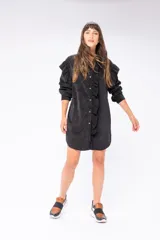 Camisa larga negra de pana fina, con cuello camisero, cierre frontal con botones, mangas largas con puños abotonados y ruedo redondeado.