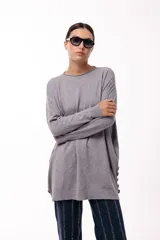 Sweater de silueta amplia y largo medio, con cuello redondo, mangas largas y detalle de botones decorativos en los laterales. Presenta un diseño de tejido de punto con caída relajada.