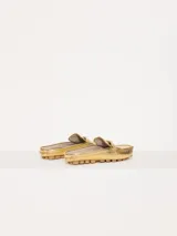 Mocasín tipo mule (destalonado) de cuero vacuno flor con textura croco, color dorado metalizado. Presenta un detalle metálico en forma de corazón sobre el empeine y suela de goma con relieve.