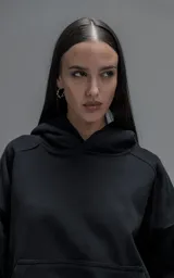 Hoodie oversize de corte crop, color negro, confeccionado en frisa gamuzada de algodón. Presenta capucha forrada, mangas largas con puños elásticos y bolsillo tipo canguro frontal.