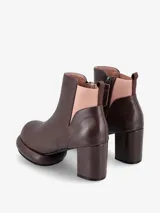 Bota corta tipo botineta de cuero negro con taco cuadrado y plataforma redondeada. Presenta un panel elástico lateral en color crema y tirador en la parte trasera.