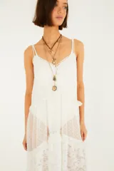 Vestido midi blanco de tirantes dobles, confeccionado con paños de tul plumeti y encaje floral. Presenta escote en V, forro corto interno, volados y un ruedo asimétrico con transparencias.