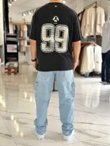 Remera regular color off-white, con diseño gráfico en la espalda que incluye el número 99 en gran tamaño y detalles en negro. Cuenta con ribetes negros en las costuras de los hombros y mangas.