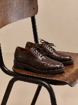 Zapato tipo oxford de cuero vacuno color marrón oscuro, con diseño de textura croco en la puntera y el talón, y detalles de perforaciones estilo brogue. Cuenta con cordones al tono y suela plana.