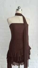 Vestido corto marrón oscuro, estilo strapless, con detalle de frunces en la cintura y falda con volados superpuestos. Incluye un accesorio tipo choker o corbatín a juego.