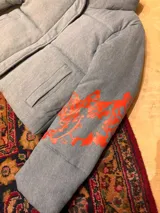 Campera puffer corta de denim azul, con cuello alto, cierre frontal oculto y bordados rojos en las mangas.