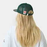 Gorra verde oscura tipo trucker con frente de cuerina, visera plana y paneles traseros de malla. Cuenta con escudo bordado en la parte frontal y cierre snapback ajustable.