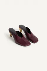 Zapato destalonado tipo mule de piel en color bordó, con escote en pico, punta cuadrada y tacón medio metalizado de diseño escultórico.