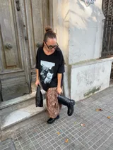 Bota de caña alta estilo biker, confeccionada en cuero sintético negro. Presenta una suela track con plataforma, puntera redondeada y un detalle de arnés con hebilla metálica y tachas en la zona del tobillo.