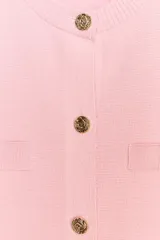 Chaqueta de punto color amarillo pálido, con cuello redondo, manga corta, cierre frontal con botones dorados y bolsillos de parche en el pecho.