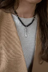 Collar de cuentas esféricas negras con detalles en metal plateado, que presenta un dije colgante en forma de pluma con acabado envejecido.