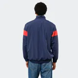 Buzo tipo rompevientos de nylon con medio cierre frontal, cuello alto y puños elásticos. Presenta un diseño en bloques de color azul, blanco y bordó, con el escudo del Club Nacional de Football y el logo de Umbro estampados en el pecho.