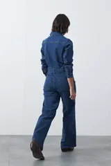 Enterito de jean negro con silueta recta y piernas amplias. Presenta cierre frontal con botones, bolsillos en el pecho y laterales, y cinturón del mismo tejido para ajustar la cintura. De manga larga con puños abotonados.