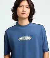 Remera de corte relajado color azul, con cuello redondo y mangas cortas. Presenta paneles laterales en color blanco con ribetes negros y un estampado frontal con el texto 'openminds' en un diseño ovalado.