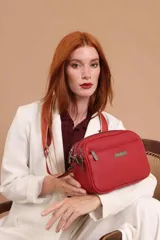 Bandolera de diseño rectangular con textura granulada, color verde oliva. Cuenta con tres compartimentos principales con cierre, un bolsillo frontal adicional y correa ancha ajustable de tela en tono a juego.