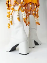 Botas de caña media de cuero sintético blanco con plataforma y tacón cuadrado. Presentan un detalle de cuentas de madera y cordón amarillo alrededor de la caña.