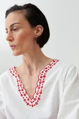 Blusa blanca de lino con bordados rojos en cuello, mangas y ruedo, de corte holgado y manga larga.