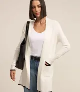 Cardigan de punto color blanco con detalles en negro en los bordes de los bolsillos, puños y ruedo. Presenta un diseño abierto, corte alargado y mangas largas.