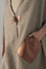 Chal de lana fina sin teñir con diseño de cuadros sutiles, cierre frontal con alamar y bolsillos de cuero metalizado. Presenta terminaciones con flecos en el ruedo y un calce estructurado en los hombros.