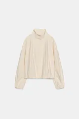 Camisa de popelín color beige, con cuello subido y manga larga acabada en puño. Cierre frontal con botones ocultos por solapa.