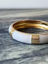 Pulsera rígida tipo brazalete, color negro con detalles dorados.