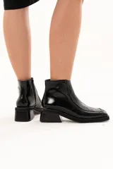 Bota corta de cuero negro con acabado brillante, diseño de punta cuadrada y taco bloque. Presenta cierre lateral interno y detalle de ribete en la capellada.