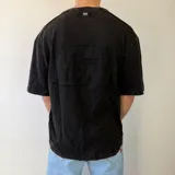 Remera oversize negra de manga corta, con efecto acid wash y gran diseño gráfico bordado o pespunteado en la espalda.