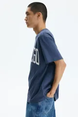 Remera de algodón de peso medio, color azul, con cuello redondo ribeteado, hombros caídos, bajo recto y corte holgado. Presenta un estampado frontal con la inscripción "SAN DIEGO" en blanco con efecto desgastado.